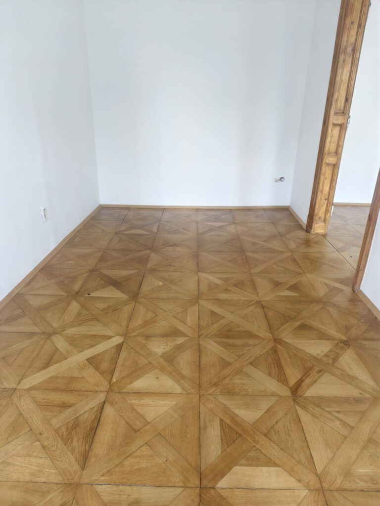 Fertig saniertes Tafelparkett mit neu montierten Massivholz-Sockelleisten in einem Altbauraum in Graz