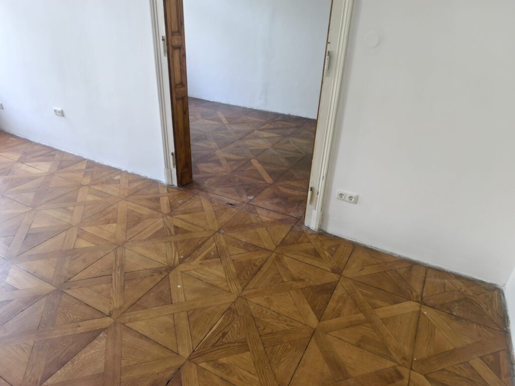 Blick durch die Flügeltür über die durchgehende Tafelparkett-Fläche zweier Altbauräume