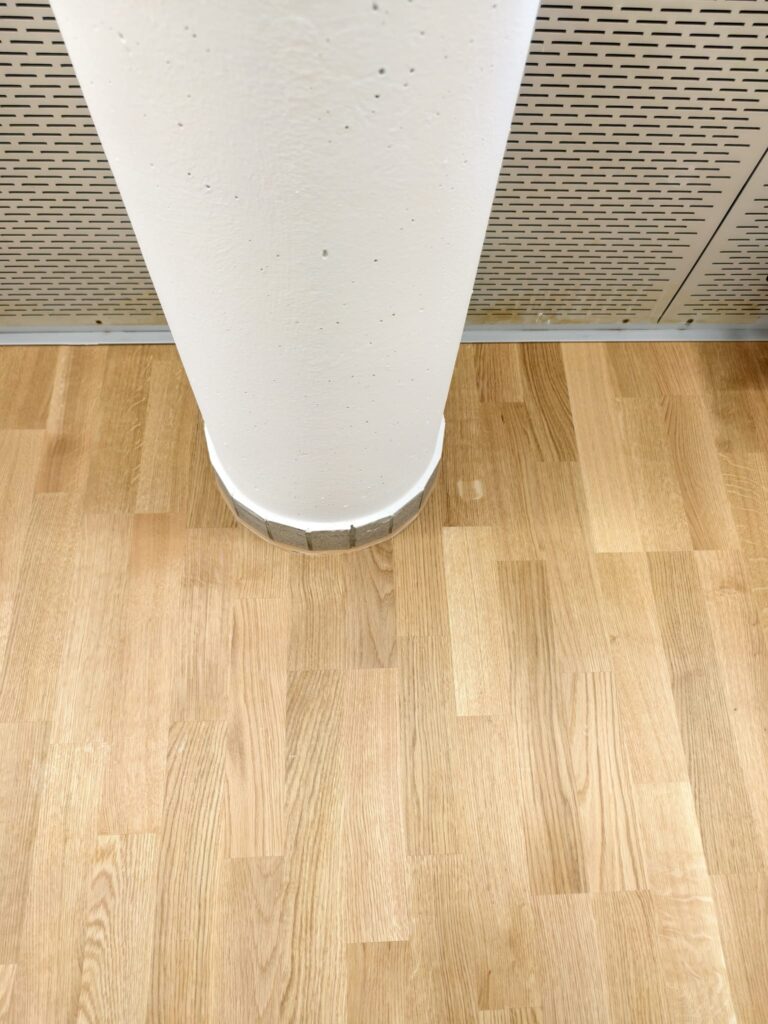 Detailaufnahme des präzise eingepassten Eichenparketts rund um eine Betonsäule